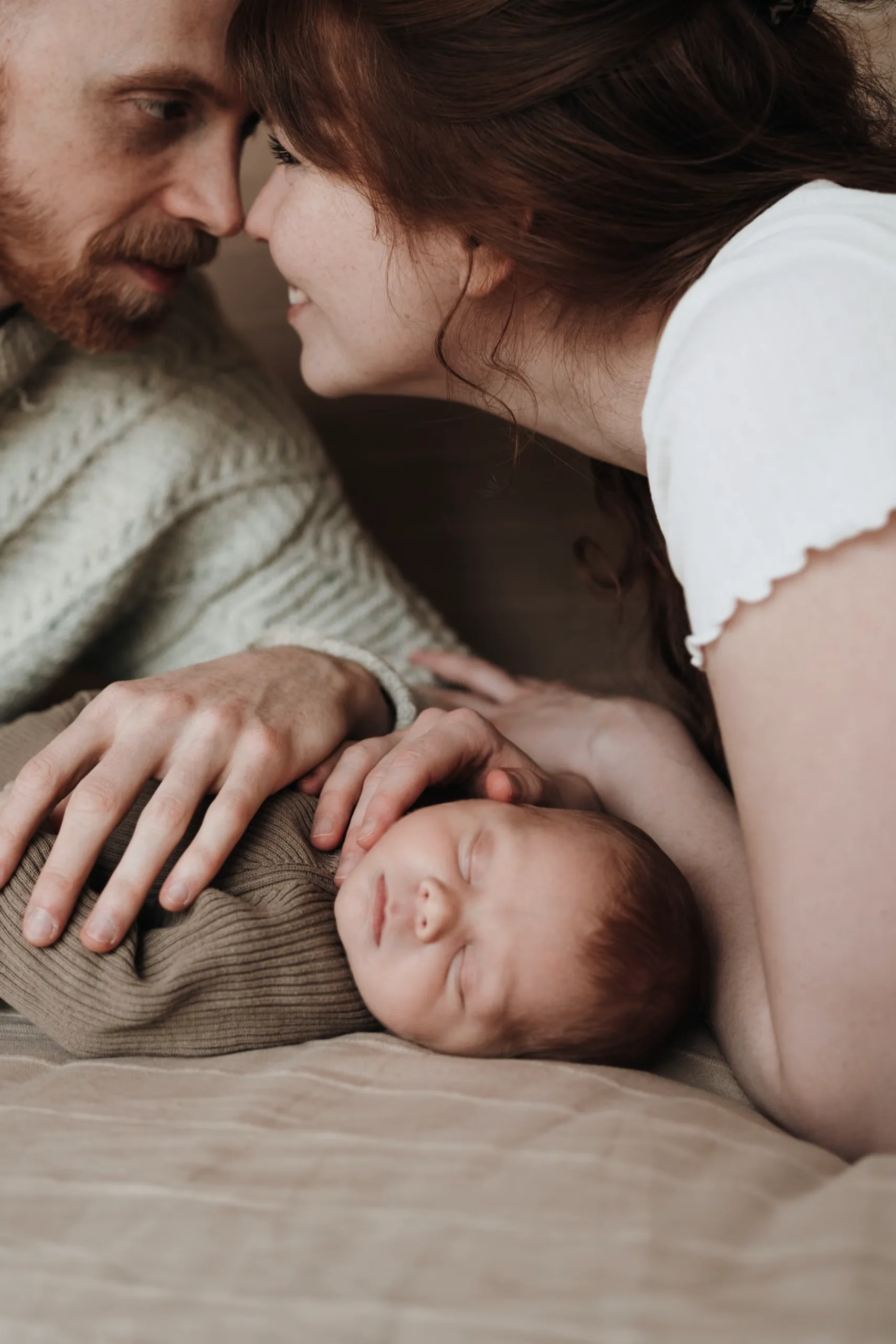 Eltern kuscheln sich nah an ihr schlafendes Neugeborenes